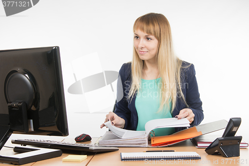 Image of Office Specialist leafing through paper documents folder looked into the computer