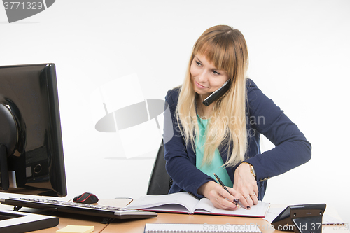 Image of Business woman talking on the phone, record information in the office book and looked at the monitor