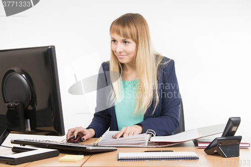 Image of Office employee working at the computer and a folder of paper documents