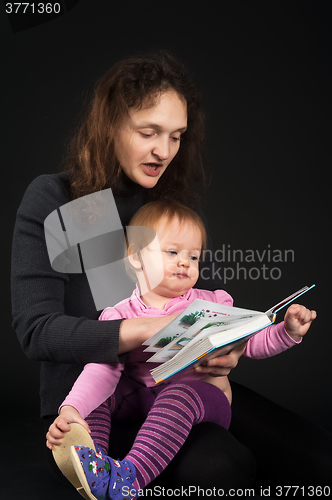 Image of mother with daughter reading book over black