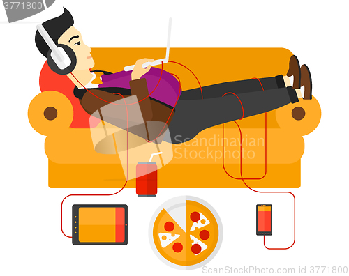 Image of Man with gadgets lying on sofa.