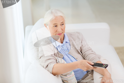 Image of senior woman with remote watching tv at home