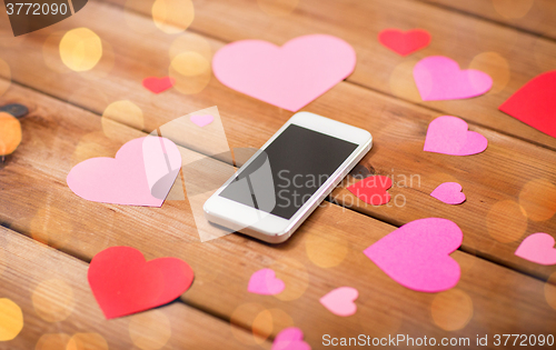 Image of close up of smartphone and hearts on wood