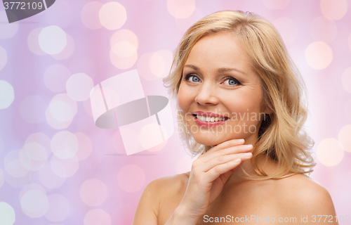 Image of smiling woman with bare shoulders touching face