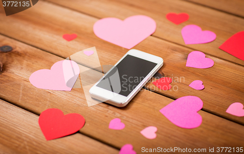 Image of close up of smartphone and hearts on wood