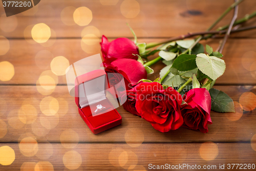 Image of close up of diamond engagement ring and red roses