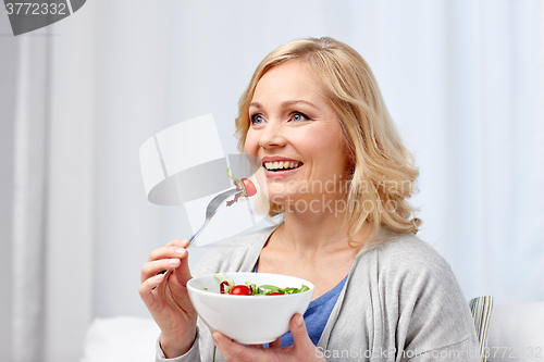 Image of smiling middle aged woman eating salad at home