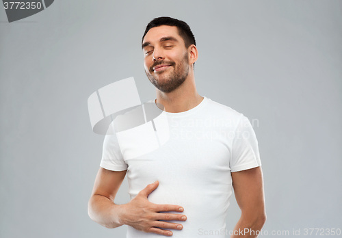 Image of happy full man touching tummy over gray background