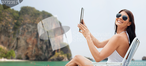 Image of smiling woman with tablet pc sunbathing on beach