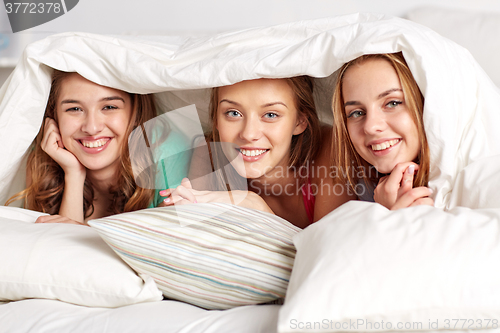 Image of happy young women in bed at home pajama party