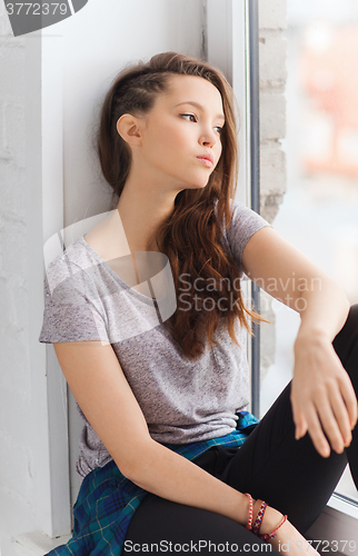 Image of sad pretty teenage girl sitting on windowsill