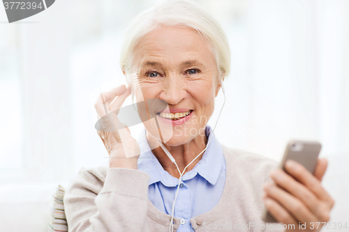 Image of senior woman with smartphone and earphones at home