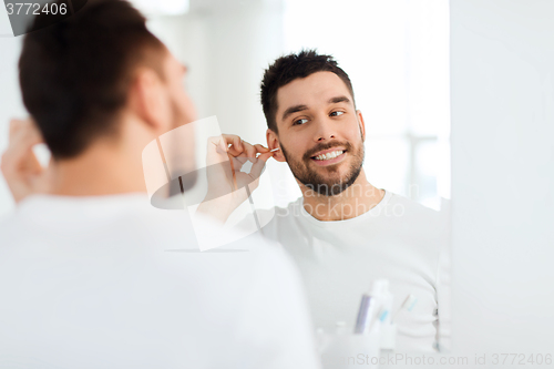 Image of man cleaning ear with cotton swab at bathroom