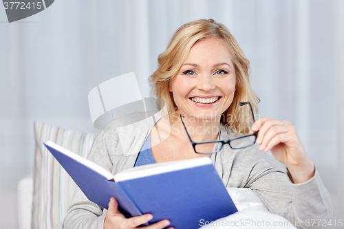 Image of smiling woman reading book and sitting on couch