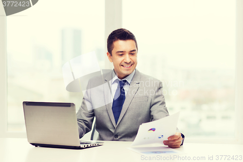 Image of smiling businessman with laptop and papers