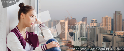 Image of sad pretty teenage girl sitting on windowsill