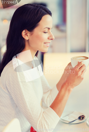 Image of smiling young woman drinking coffee at cafe