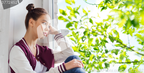 Image of sad pretty teenage girl sitting on windowsill