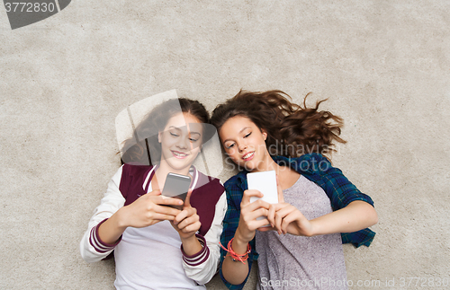 Image of happy teenage girls lying on floor with smartphone