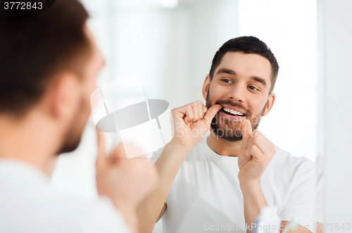 Image of man with dental floss cleaning teeth at bathroom