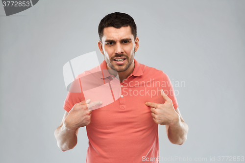 Image of angry man pointing finger to himself over gray