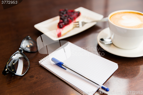 Image of close up of notebook with pen, coffee cup and cake