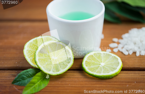 Image of close up of body lotion in cup and limes on wood