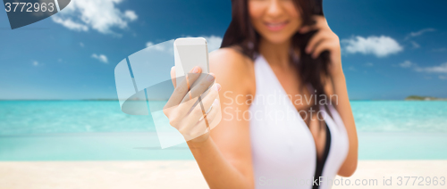 Image of young woman taking selfie with smartphone on beach