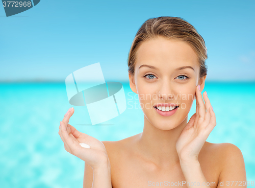 Image of happy young woman applying cream to her face