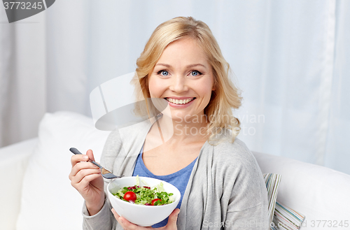 Image of smiling middle aged woman eating salad at home