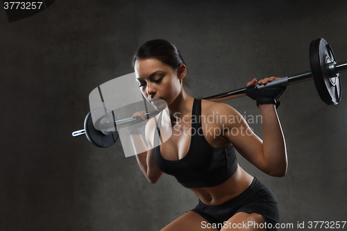 Image of young woman flexing muscles with barbell in gym