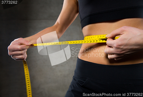 Image of close up of woman measuring waist by tape in gym