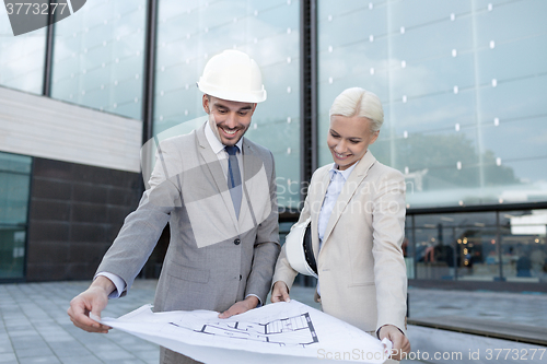 Image of smiling businessmen with blueprint and helmets