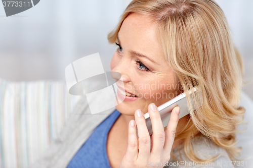 Image of smiling woman calling on smartphone at home