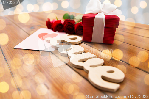 Image of close up of gift box, red roses and greeting card