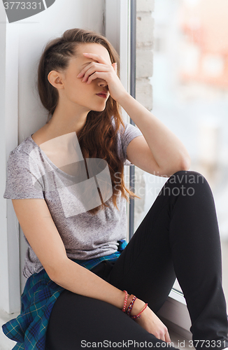 Image of sad pretty teenage girl sitting on windowsill