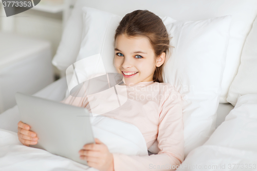 Image of happy girl lying in bed with tablet pc at home