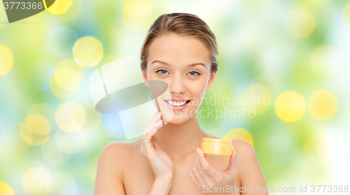 Image of happy young woman applying cream to her face