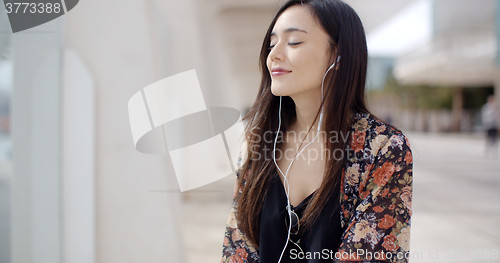 Image of Trendy young woman listening to music in town