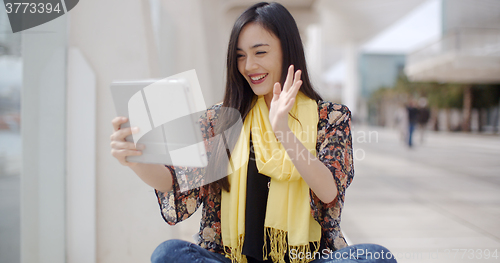 Image of Smiling woman waving at her tablet computer