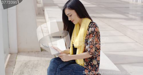 Image of Young woman sitting reading her tablet