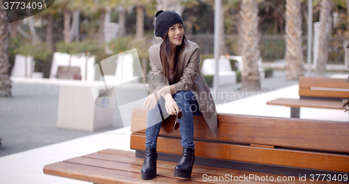 Image of Fashionable young woman sitting waiting on a bench