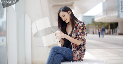 Image of Young woman sitting reading a text message