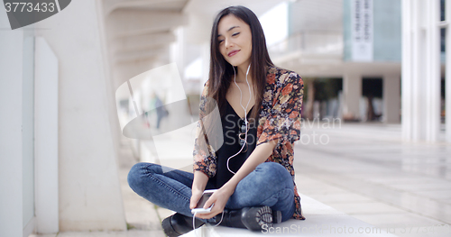 Image of Trendy young woman listening to music in town