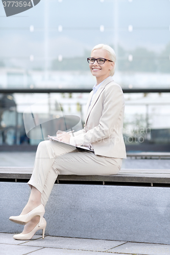 Image of young smiling businesswoman with notepad outdoors