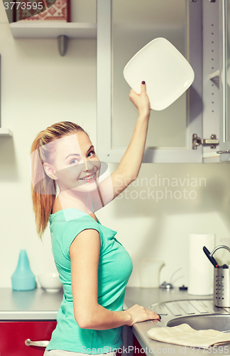 Image of happy woman putting plate to kitchen cabinet