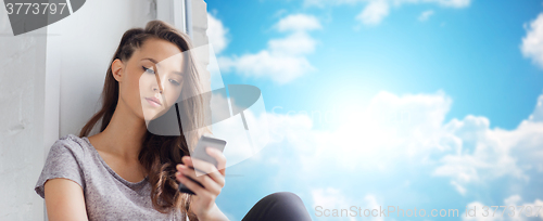 Image of sad pretty teenage girl with smartphone texting