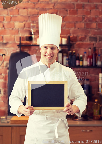 Image of happy male chef with blank menu board in kitchen