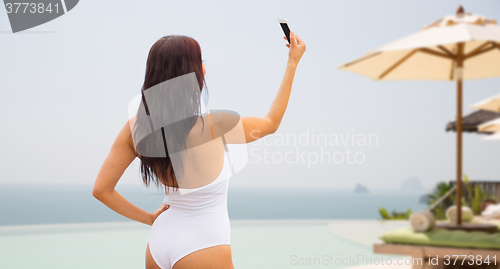 Image of young woman taking selfie with smartphone on beach