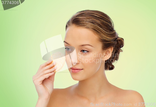 Image of young woman cleaning face with exfoliating sponge